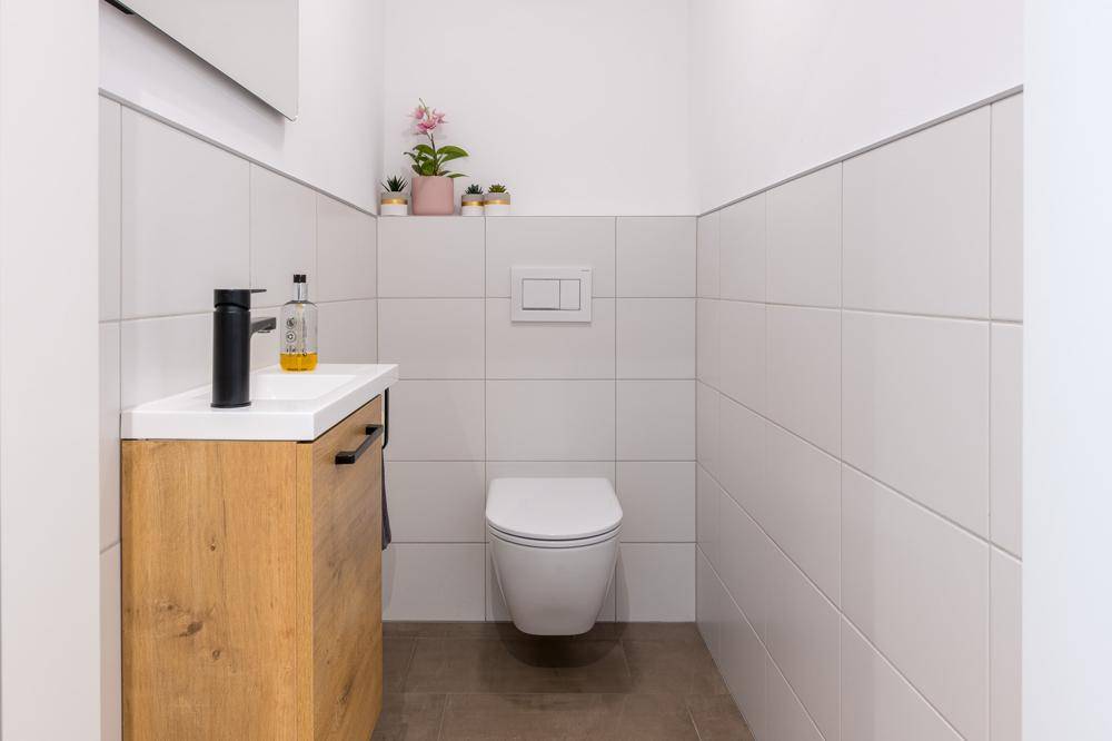 Modernes Gäste-WC mit wandhängender Toilette und kleinem Waschbeckenunterschrank.