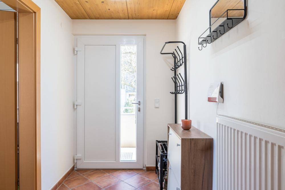 Heller Eingangsbereich mit Terrakottafliesen, Garderobe und weißer Eingangstür mit Glaseinsatz.