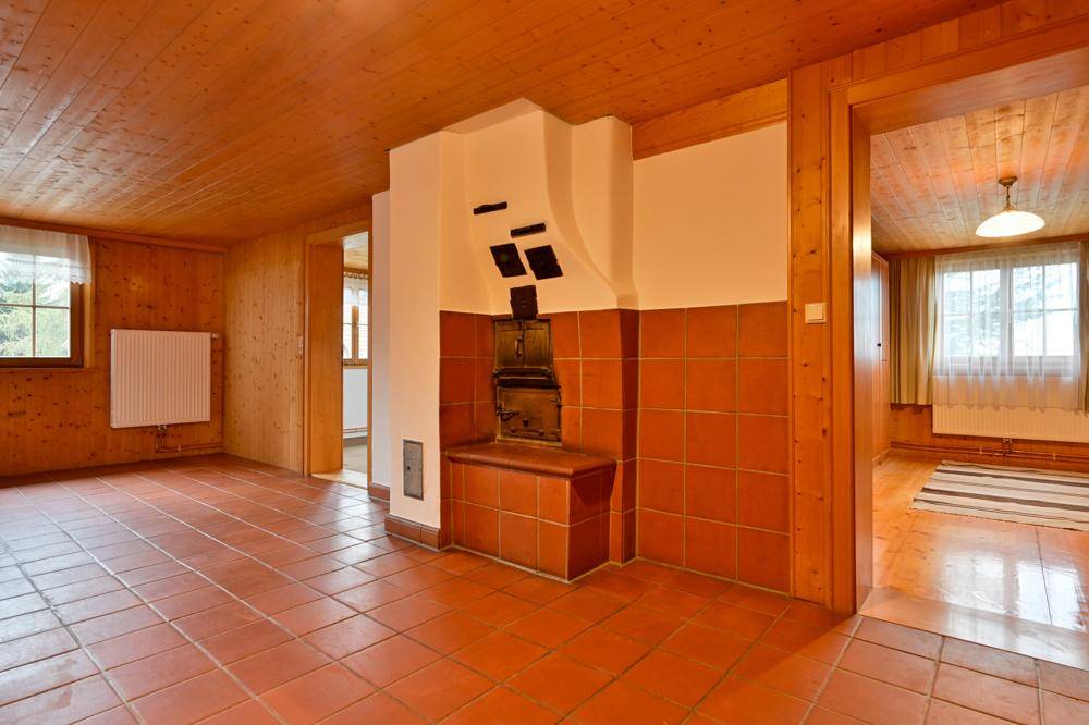 Geräumiger Wohnbereich mit Terrakottafliesen, Holzwänden und einem traditionellen Kachelofen.