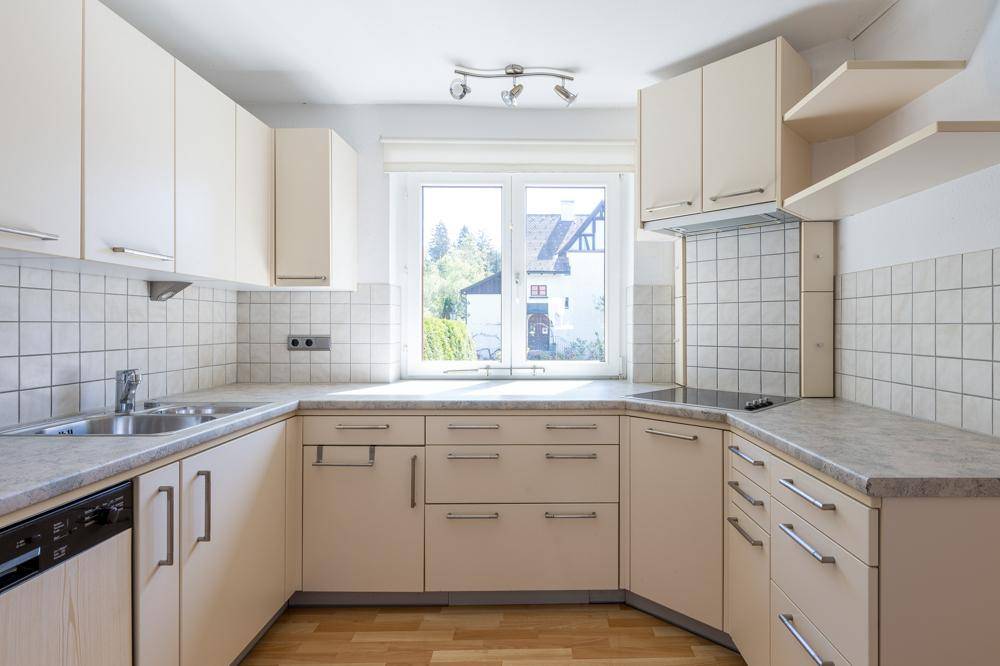 Helle Küche mit beigefarbenen Einbauschränken, Fliesenrückwand und Fenster mit Blick ins Grüne.