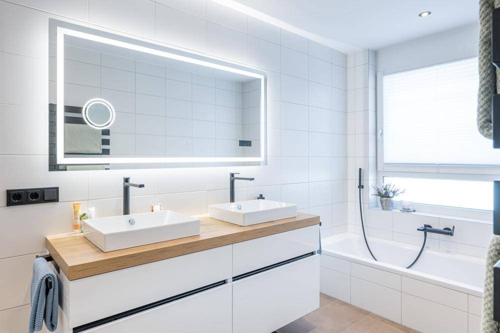 Modernes Badezimmer mit Doppelwaschbecken, beleuchtetem Spiegel und Badewanne.