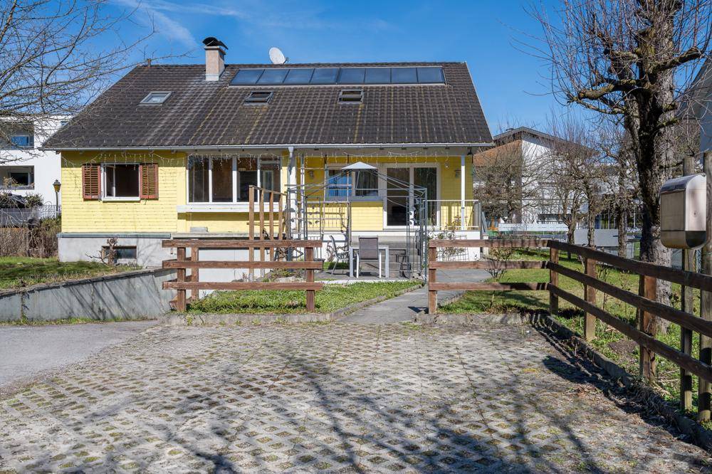Rückansicht des gelben Einfamilienhauses mit Parkplatz und Holzzaun.