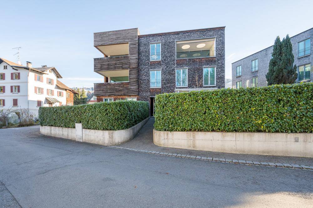 Moderne Wohnanlage mit Holzfassade, gepflegter Hecke und barrierefreiem Zugang.