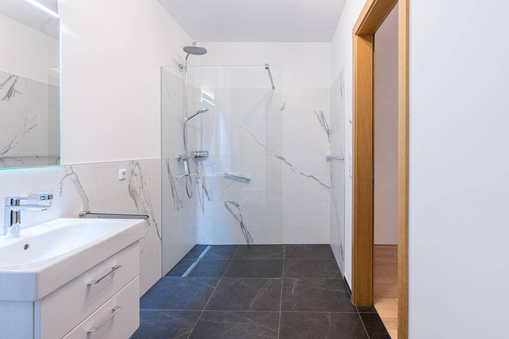 Modernes Badezimmer mit ebenerdiger Dusche, Einzelwaschbecken und Marmorfliesen.