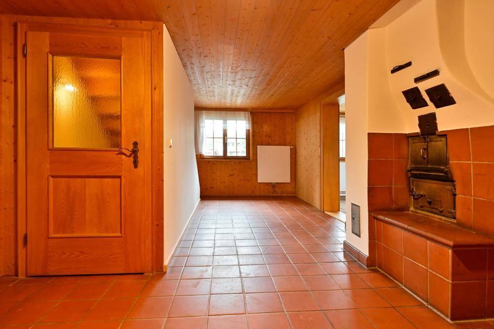 Flur mit Terrakottafliesen, Holztür und einem traditionellen Kachelofen, der Wärme spendet.