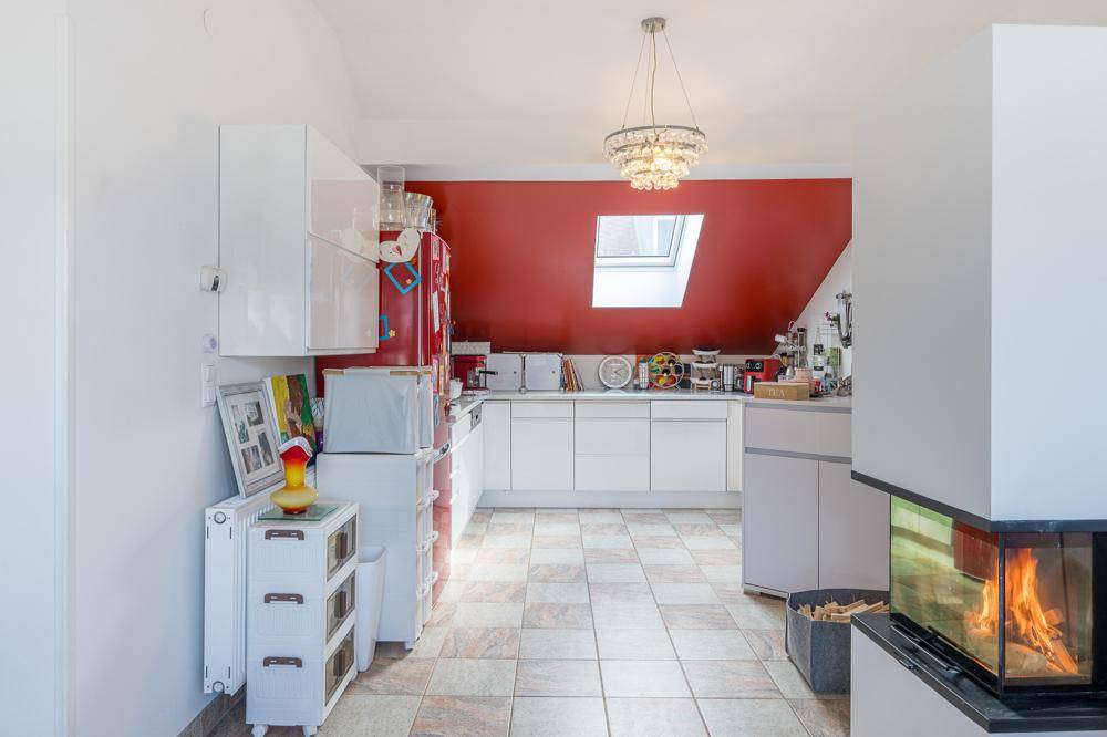 Moderne Küche mit weißen Schränken, roter Akzentwand, Kamin und Dachfenster.