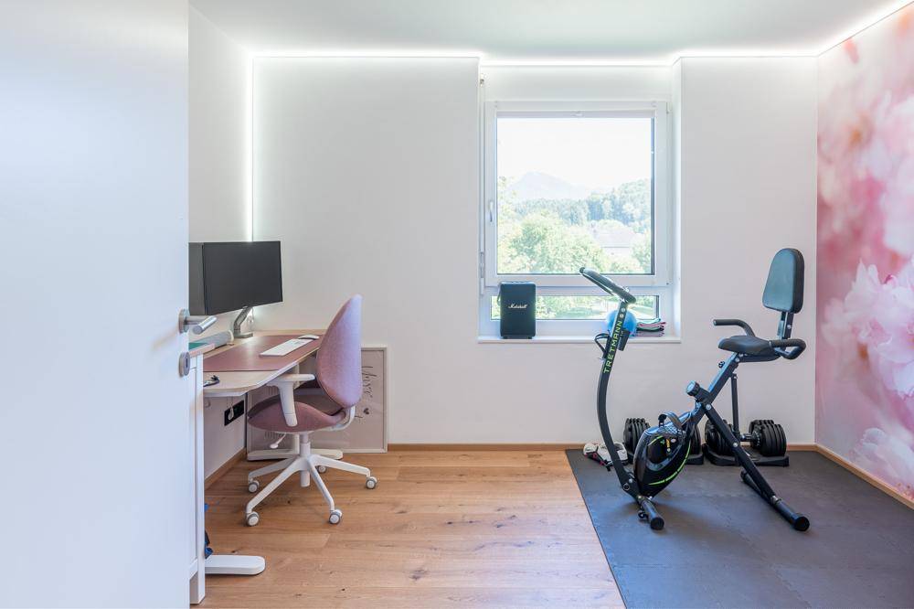 Vielseitiger Raum, genutzt als Büro und Fitnessbereich, mit Blick ins Grüne.