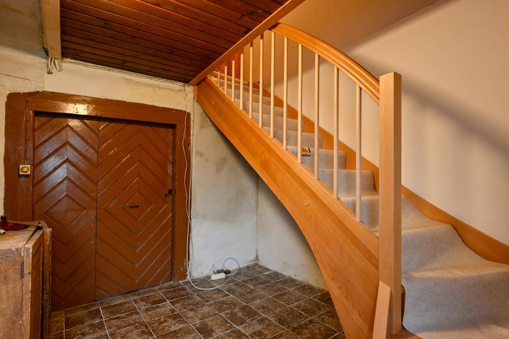 Treppenhaus mit Holztreppe, Teppichstufen und einer rustikalen Holztür.