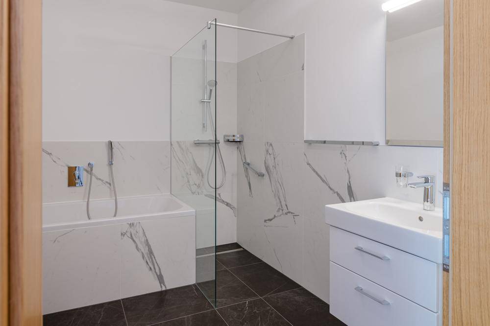 Modernes Badezimmer mit Badewanne, Dusche und eleganten Marmorfliesen.