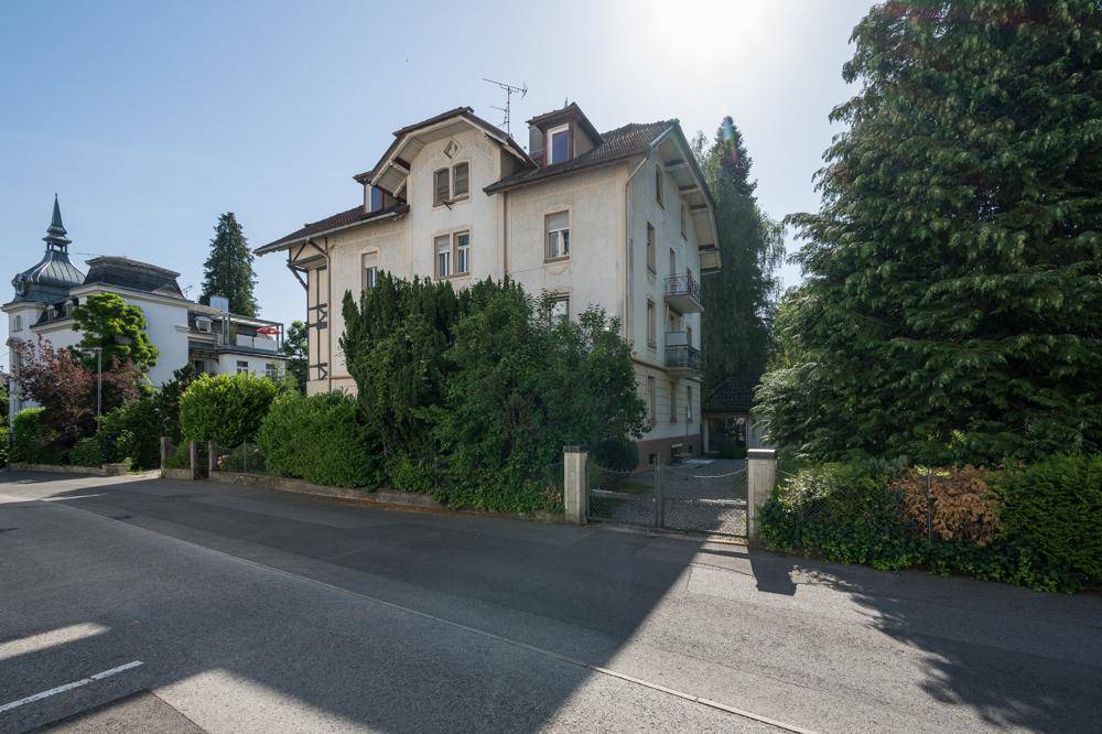 Klassisches Gebäude mit traditioneller Architektur und üppiger Bepflanzung an einer Straße.