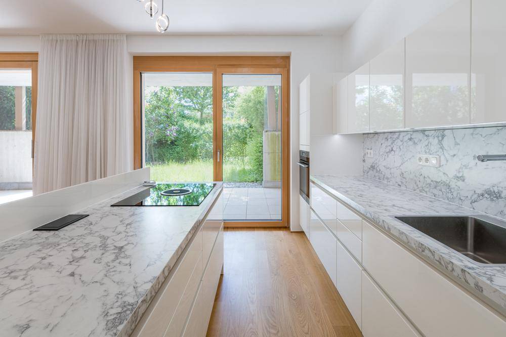 Moderne Einbauküche mit Marmorarbeitsplatten, Induktionskochfeld und Zugang zum Garten.