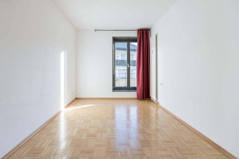 Gemütliches Zimmer mit Parkettboden und einem Fenster mit rotem Vorhang.