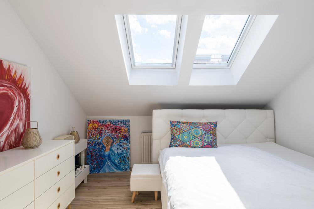 Schlafzimmer im Dachgeschoss mit Doppelbett, Kommode und zwei großen Dachfenstern.