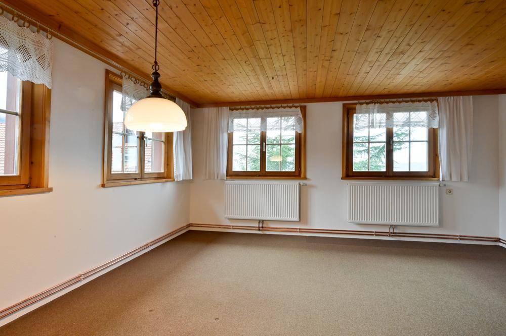 Geräumiges Zimmer mit Teppichboden, Holzdecke und mehreren Fenstern mit Spitzenvorhängen.