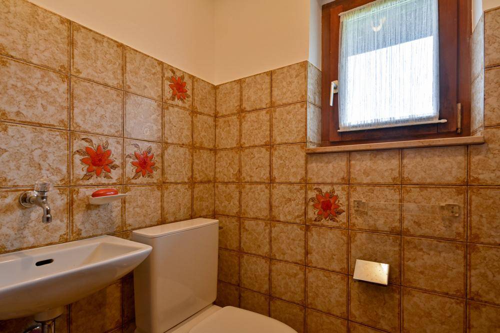 Kleines WC mit floral gemusterten Fliesen, Toilette, Waschbecken und Fenster.