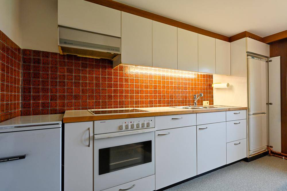 Funktionale Küche mit weißen Schränken, Holztheke und orangefarbenen Fliesen als Spritzschutz.