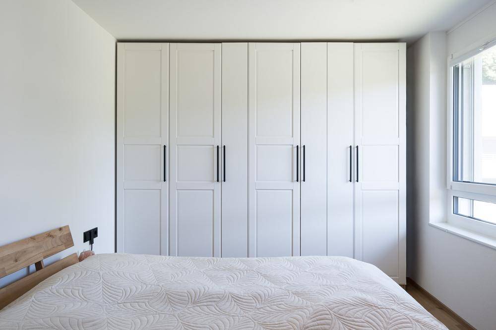 Schlafzimmer mit großem weißen Einbauschrank und hellem Fenster, das viel Tageslicht hereinlässt.