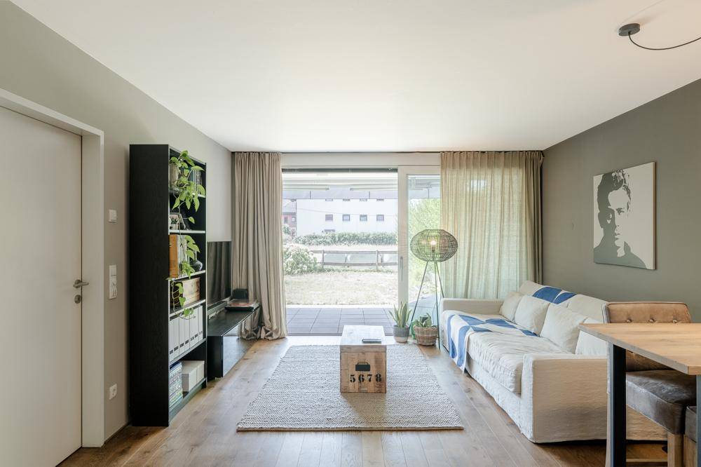 Gemütliches Wohnzimmer mit Holzboden, moderner Einrichtung und großem Schiebefenster zur Terrasse.