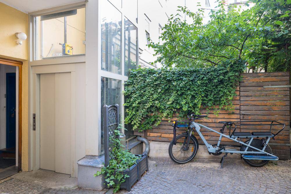 Begrünter Innenhof mit Aufzug, Fahrrad und Holzzaun.