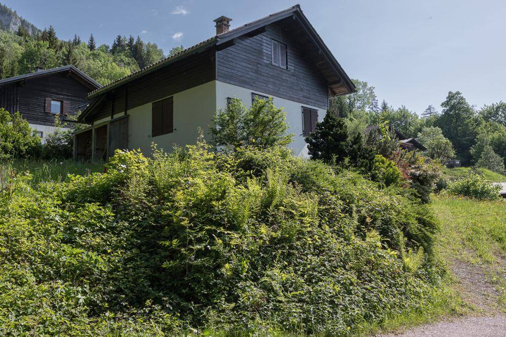 Haus mit dunkler Holzfassade und hellerem Untergeschoss, umgeben von üppiger Vegetation.