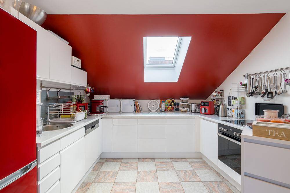 Helle Küche mit weißen Unterschränken, roter Wand, Spüle und integrierten Geräten.
