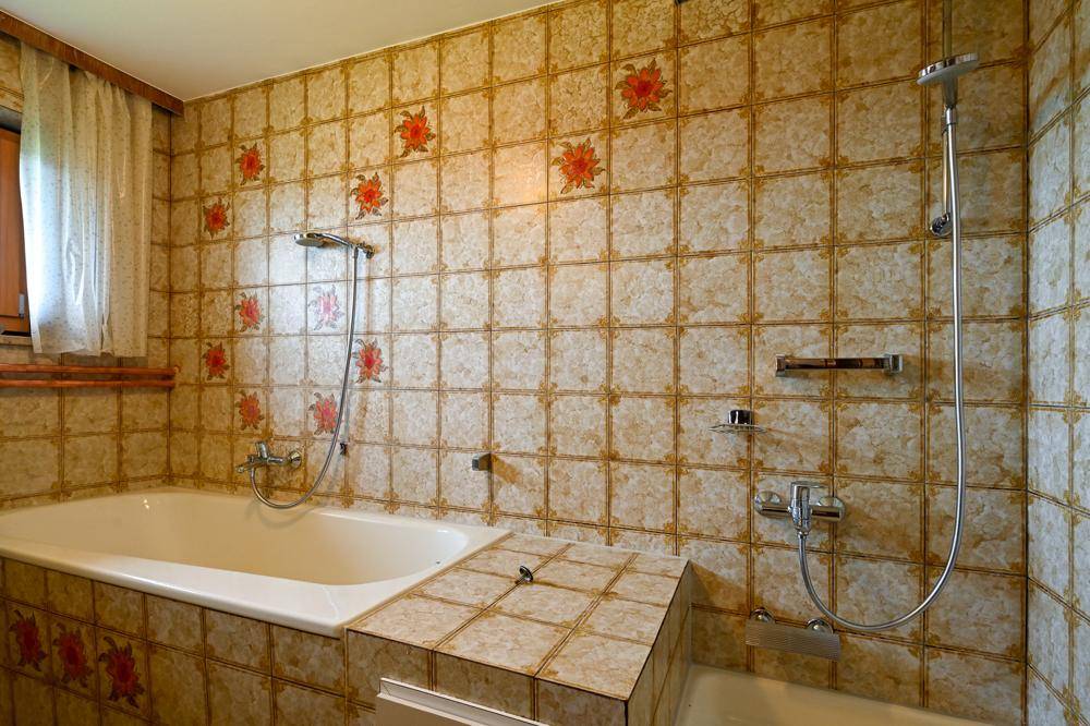 Badezimmer mit floral gemusterten Fliesen, Badewanne und Duschvorrichtung.