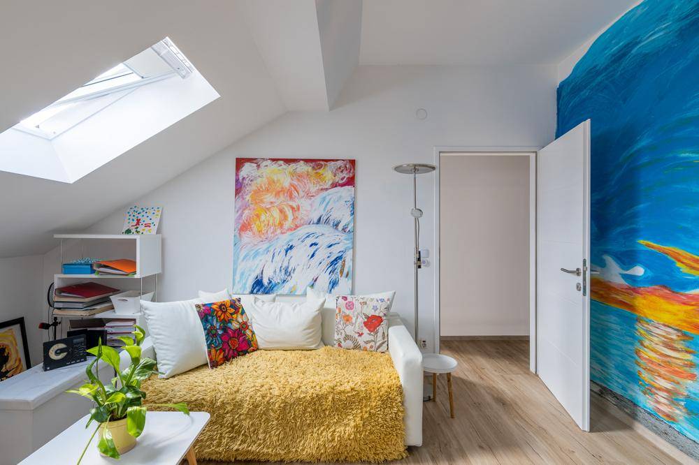 Gemütliches Schlafzimmer mit Schlafsofa, farbenfroher Wandkunst und Dachfenster.