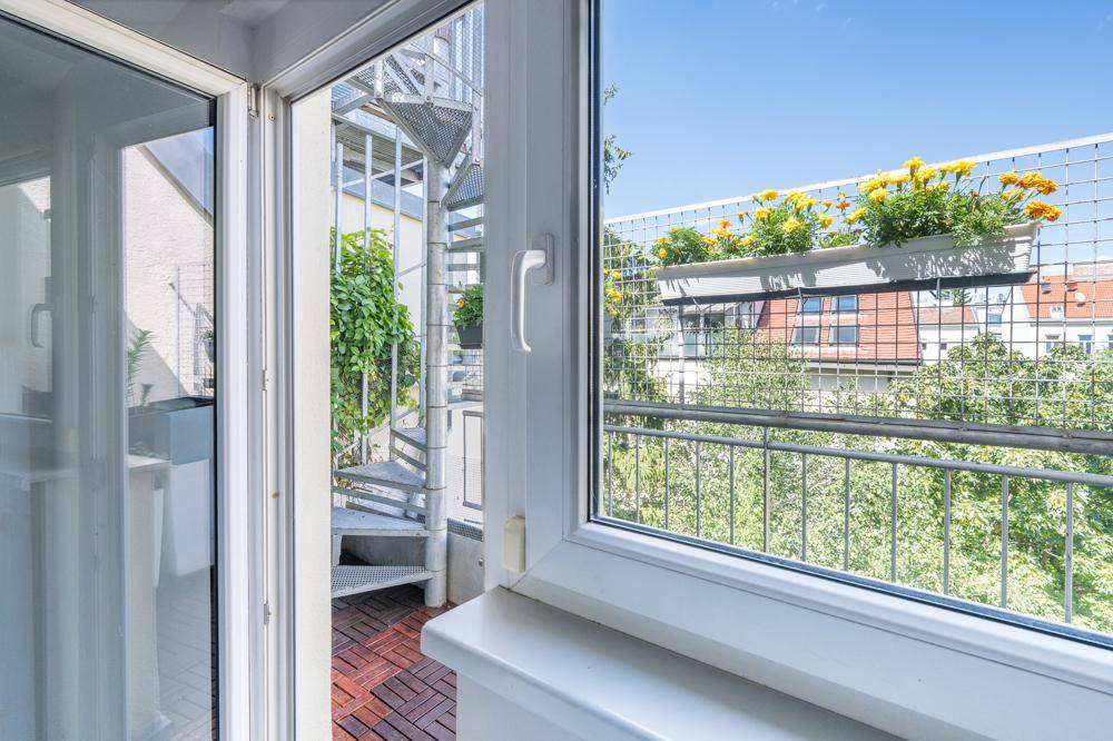 Blick aus dem Fenster auf eine Wendeltreppe, die zu einem begrünten Außenbereich führt.