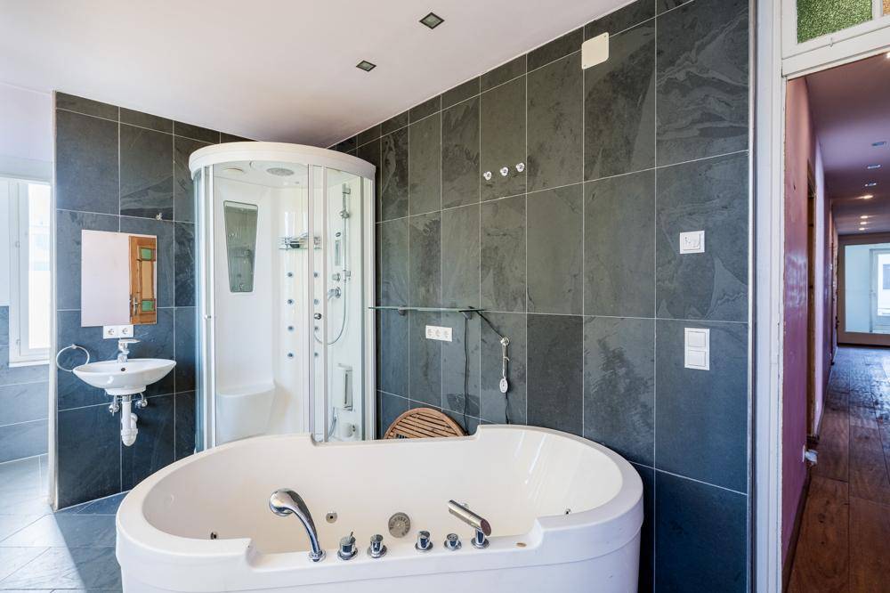 Modernes Badezimmer mit Whirlpool-Badewanne, Duschkabine und dunklen Fliesen.
