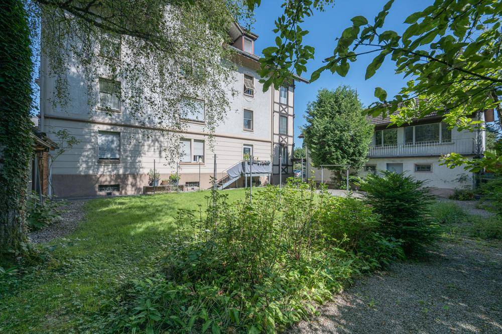 Grüner Gartenbereich hinter dem Gebäude mit Rasenfläche und Zugang zum Haus.
