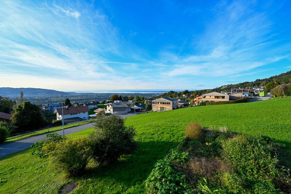 Weitläufige grüne Hügellandschaft mit Fernblick auf einen See und die umliegende Bebauung.
