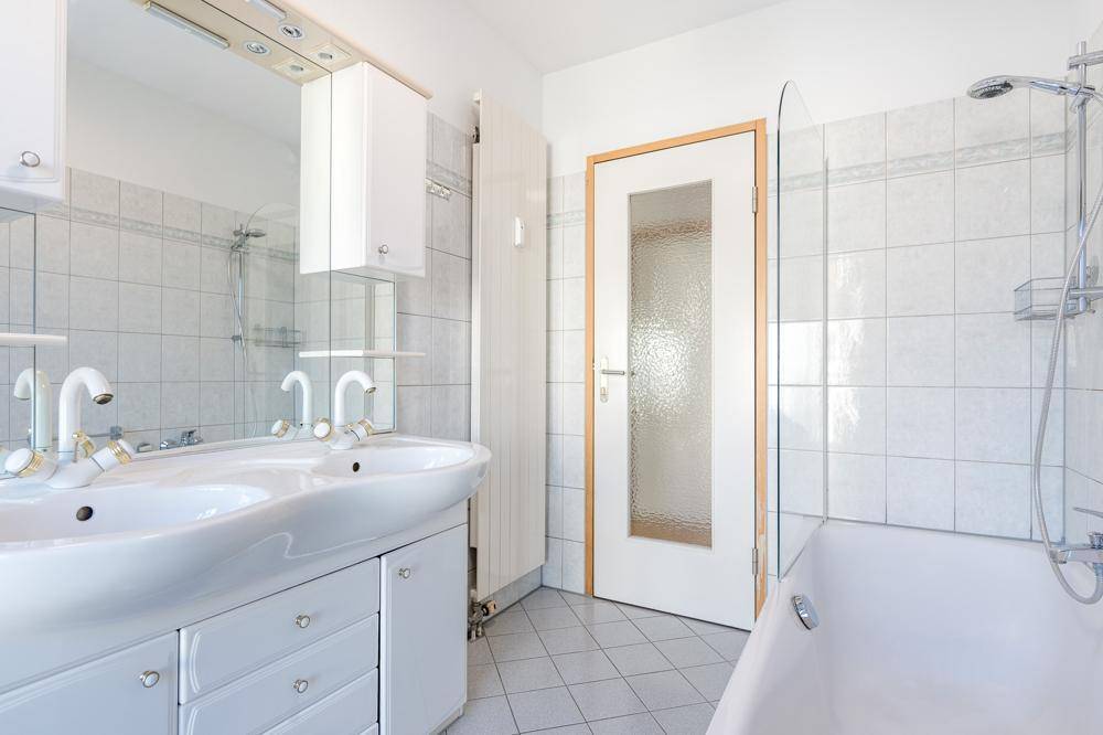 Badezimmer mit Doppelwaschbecken, Badewanne und weißen Fliesen.