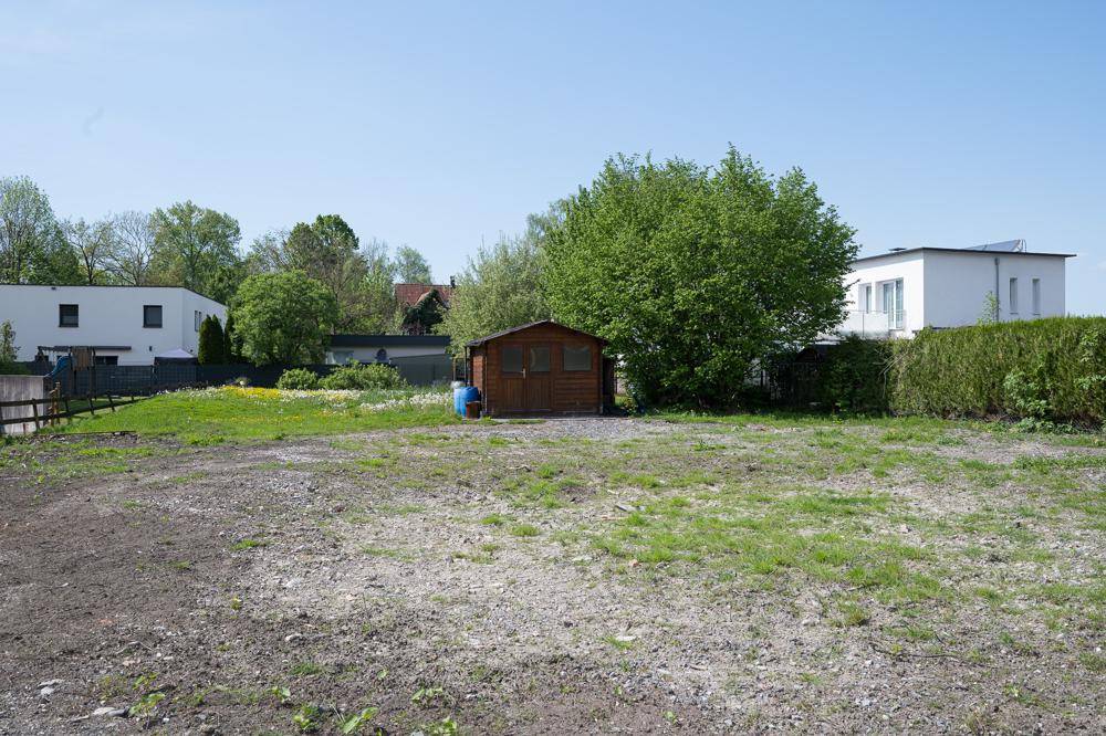 Freie Parzelle mit Kiesfläche und einem kleinen Holzschuppen, umgeben von Wohngebäuden.