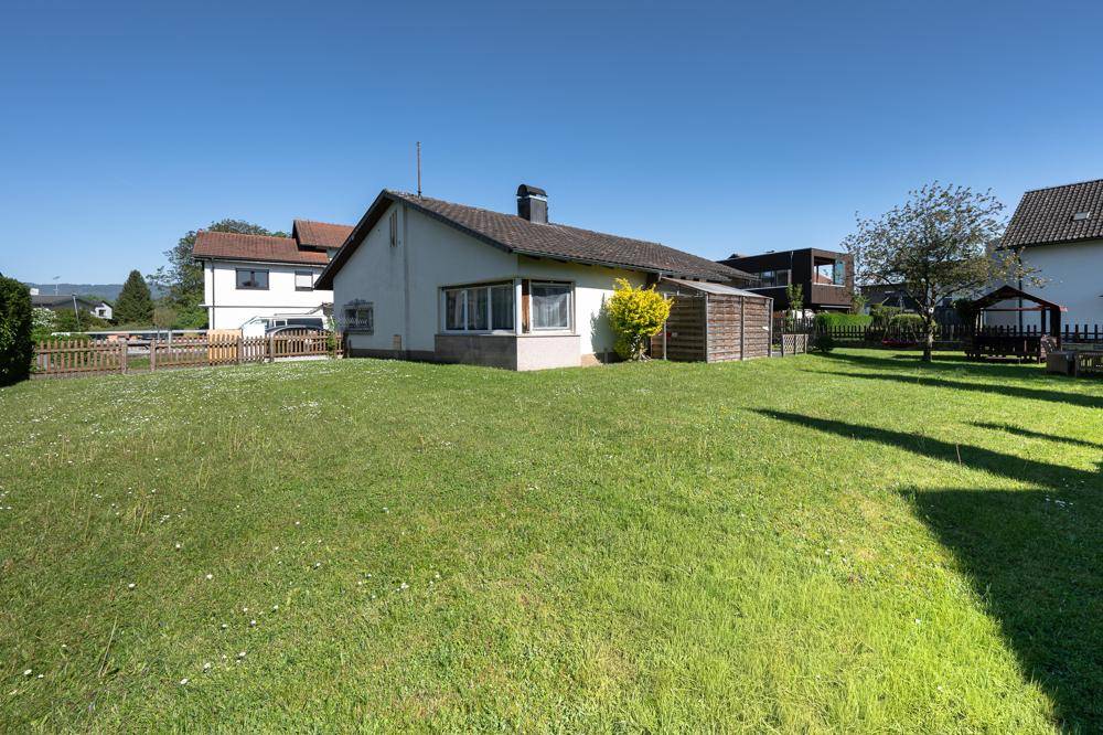 Rückseite des Hauses mit großem Garten und angrenzender Terrasse unter blauem Himmel.