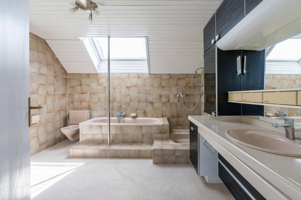 Badezimmer im Stil der 80er Jahre mit beigefarbenen Fliesen, Badewanne und Dachfenstern.