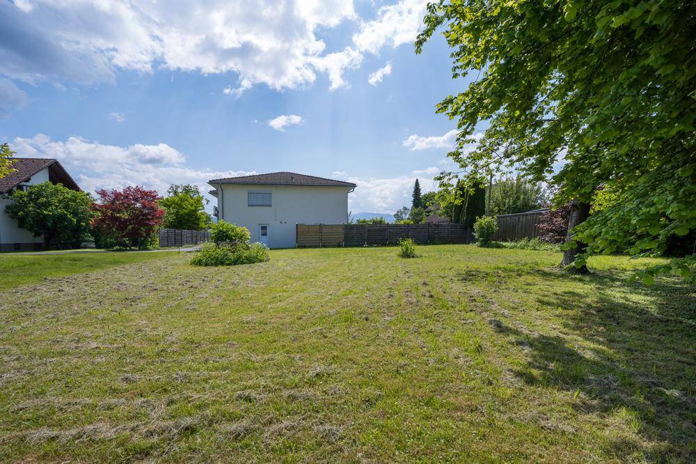 Gepflegte Rasenfläche mit Bäumen und Blick auf die Rückseite eines modernen Hauses.