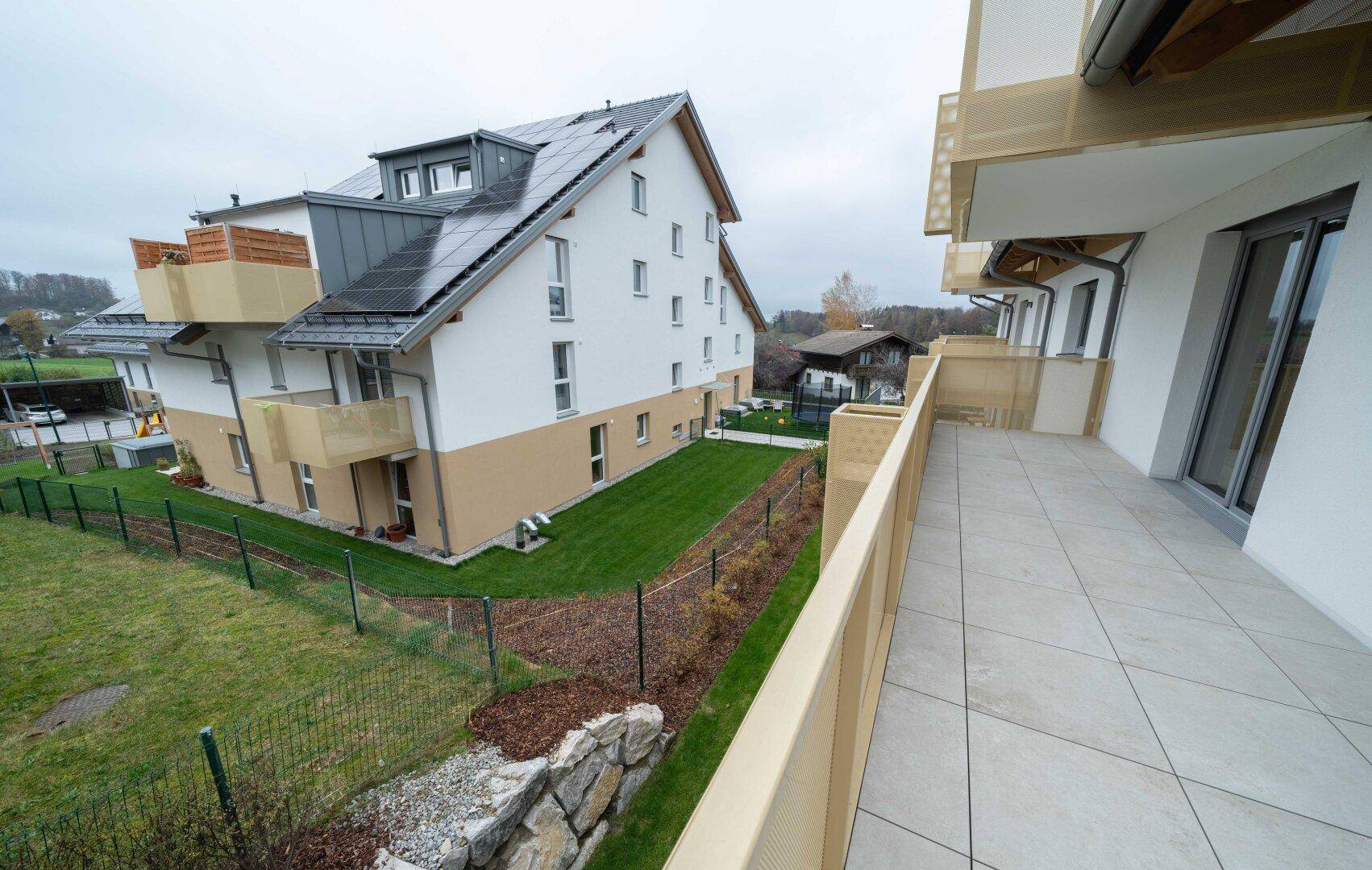 Geräumiger Balkon mit Fliesenboden und Blick auf den Garten und das Nachbargebäude.