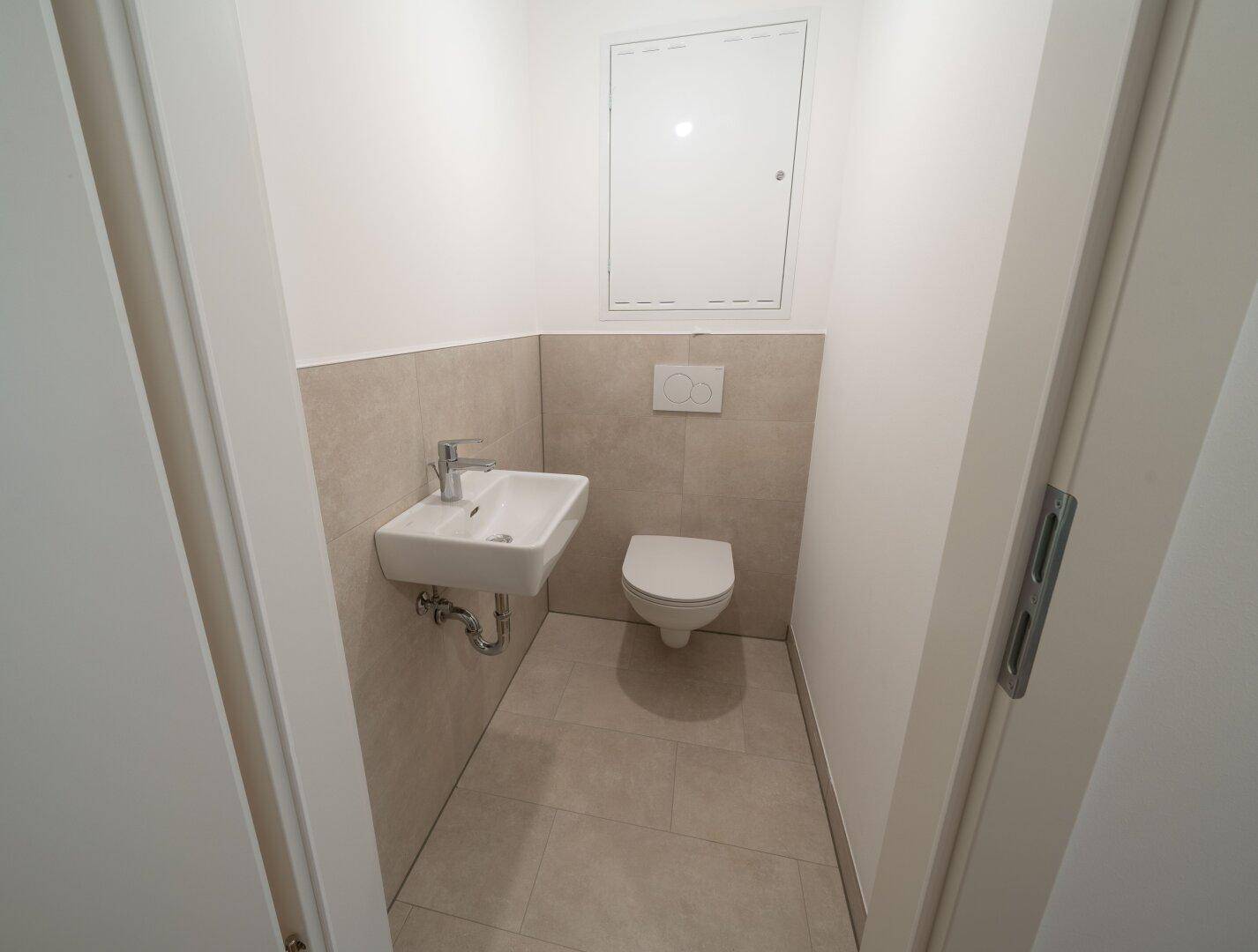 Kleines Gäste-WC mit wandhängendem WC und Handwaschbecken in neutralen Farbtönen.