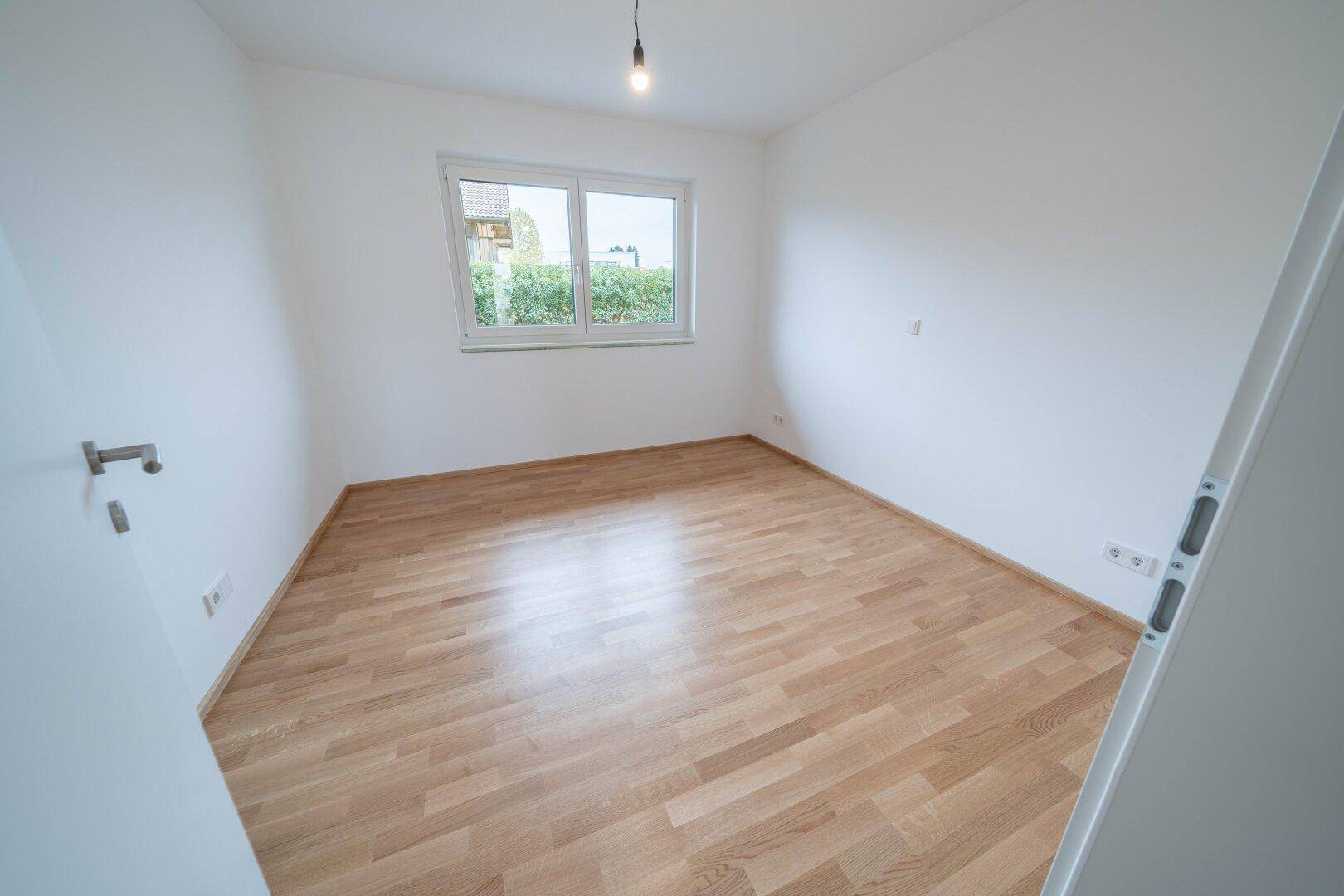 Helles Schlafzimmer mit Parkettboden und einem Fenster, das viel Tageslicht hereinlässt.