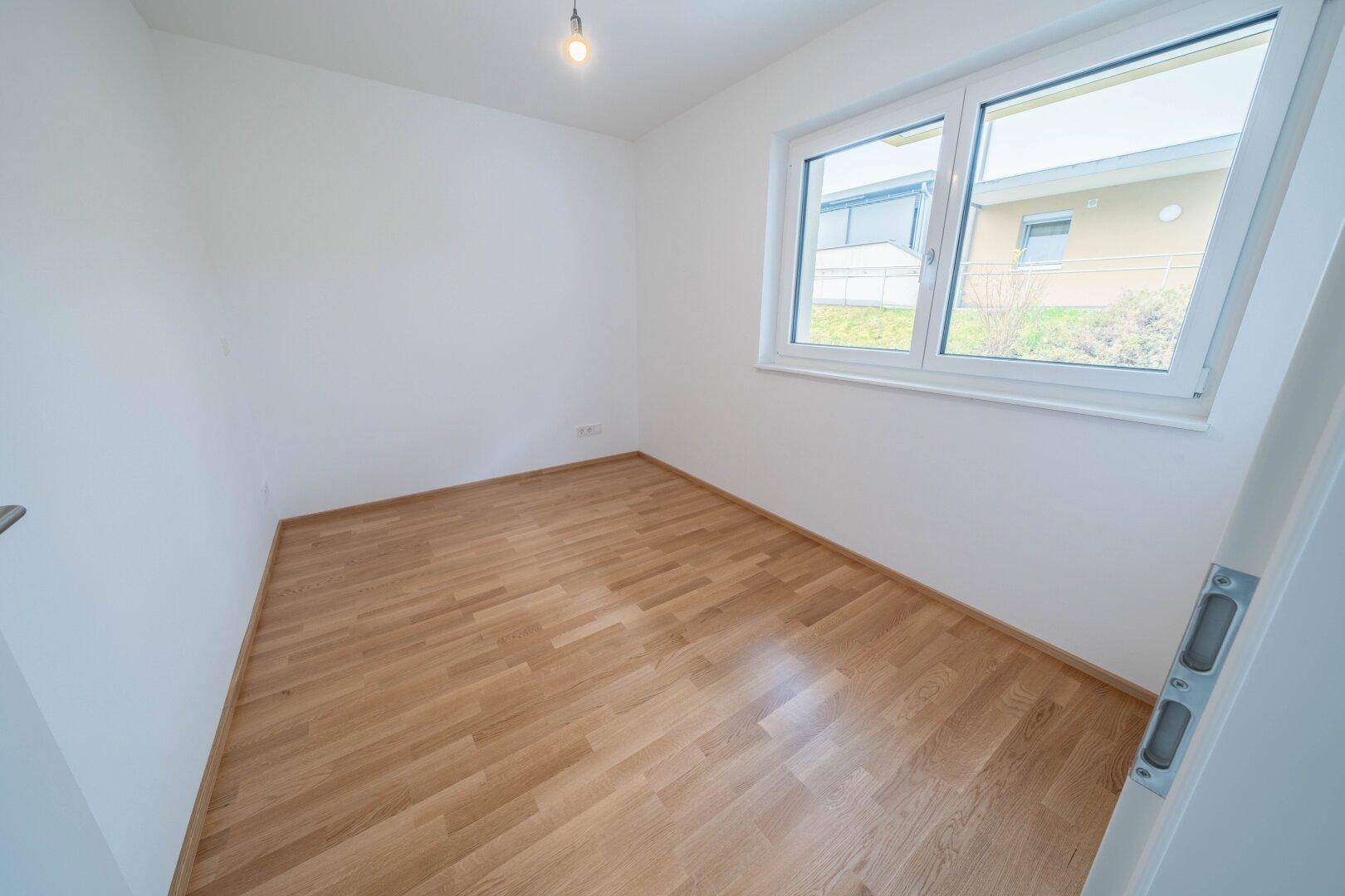 Freundliches Zimmer mit Parkettboden und einem großen Fenster, ideal als Schlaf- oder Kinderzimmer.