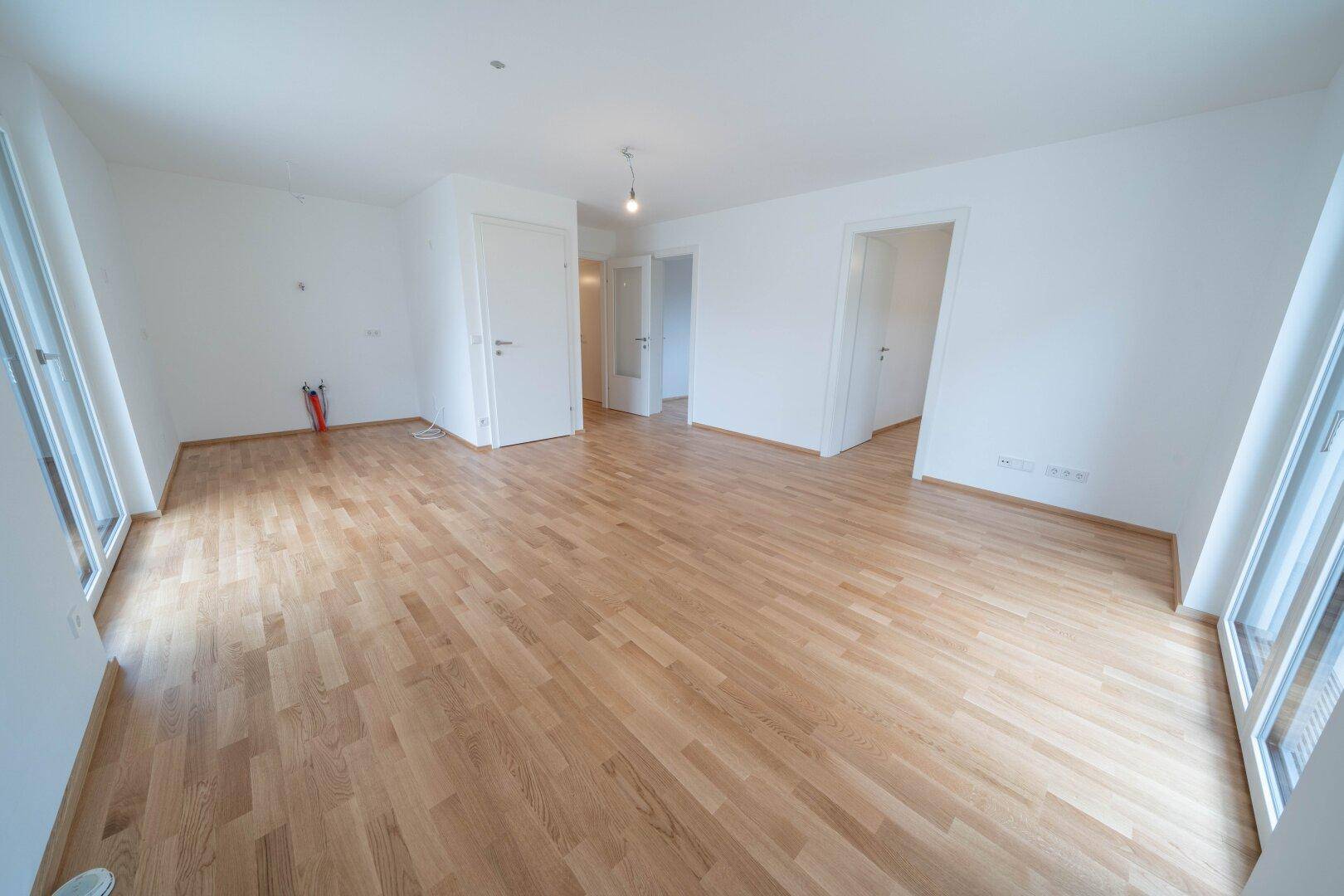 Geräumiges, helles Wohnzimmer mit Parkettboden und großen Fenstern für viel Tageslicht.