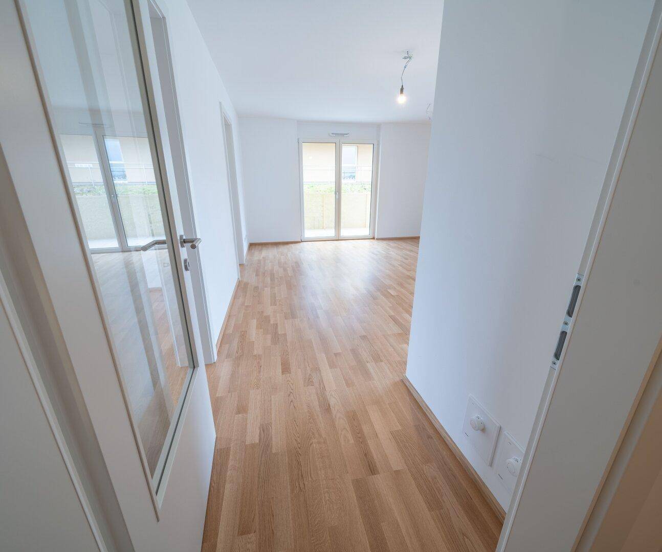 Langer, heller Flur mit Parkettboden und Zugang zu einem Balkon am Ende des Ganges.