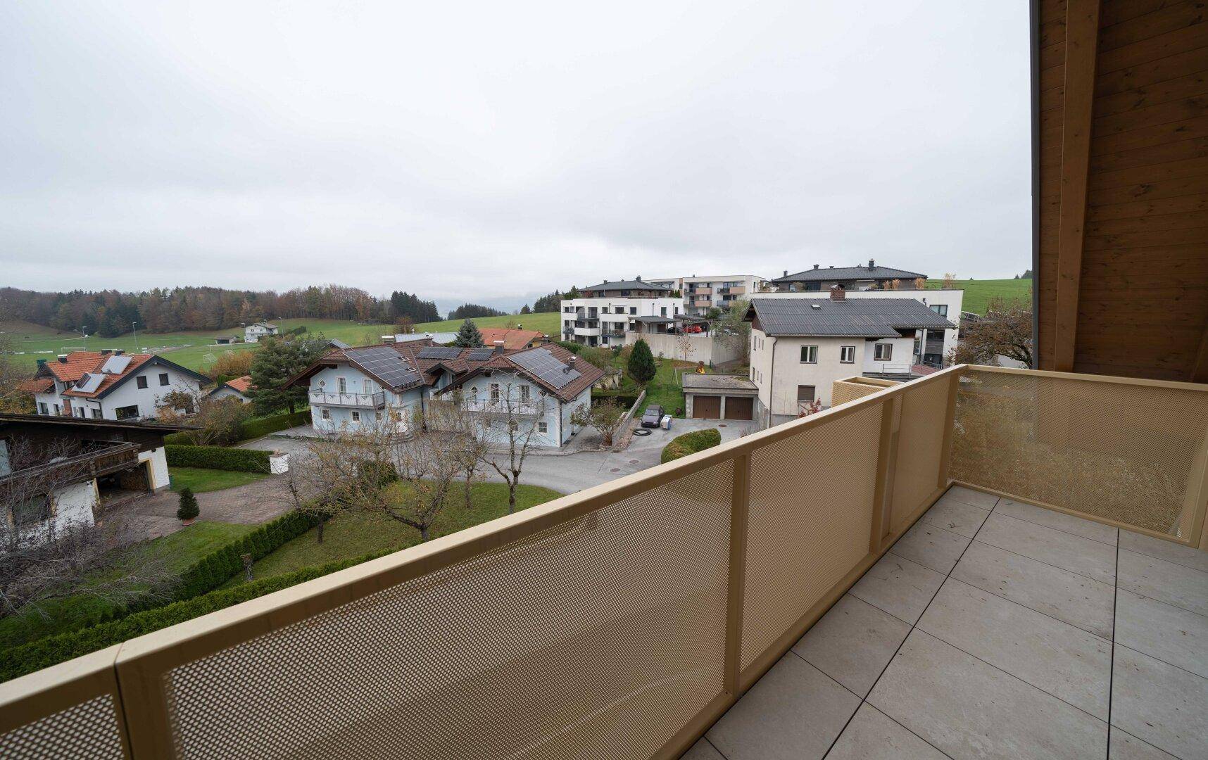 Balkon mit Fliesenboden und weitem Blick über die grüne Landschaft und umliegende Häuser.