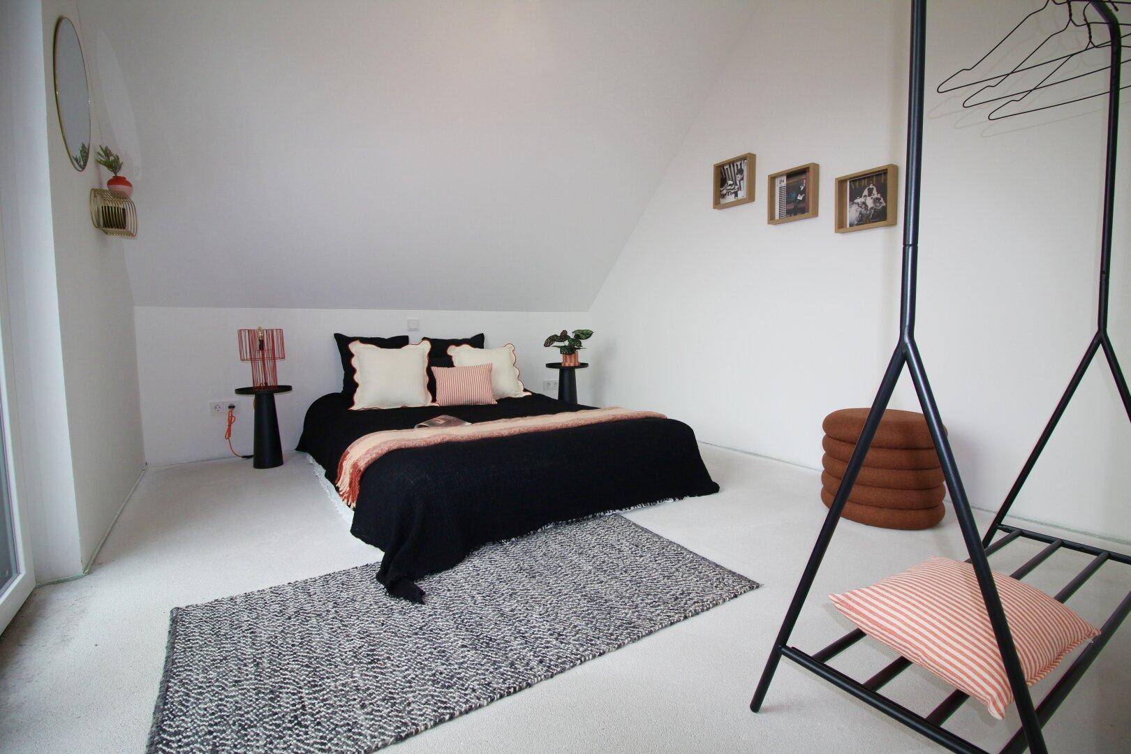 Modernes Schlafzimmer mit schwarzem Bett, Dachschräge und minimalistischer Dekoration.