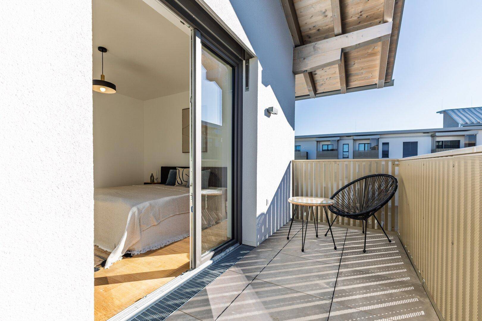 Balkon mit Blick in ein Schlafzimmer, ausgestattet mit einem modernen Stuhl und Holzboden.