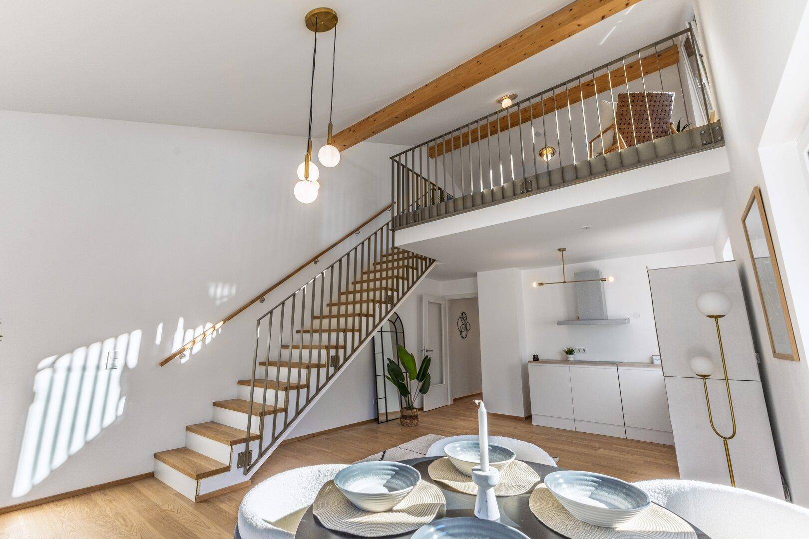 Geräumiger Wohn- und Essbereich mit offener Küche, Treppe zur Galerie und hohen Decken.