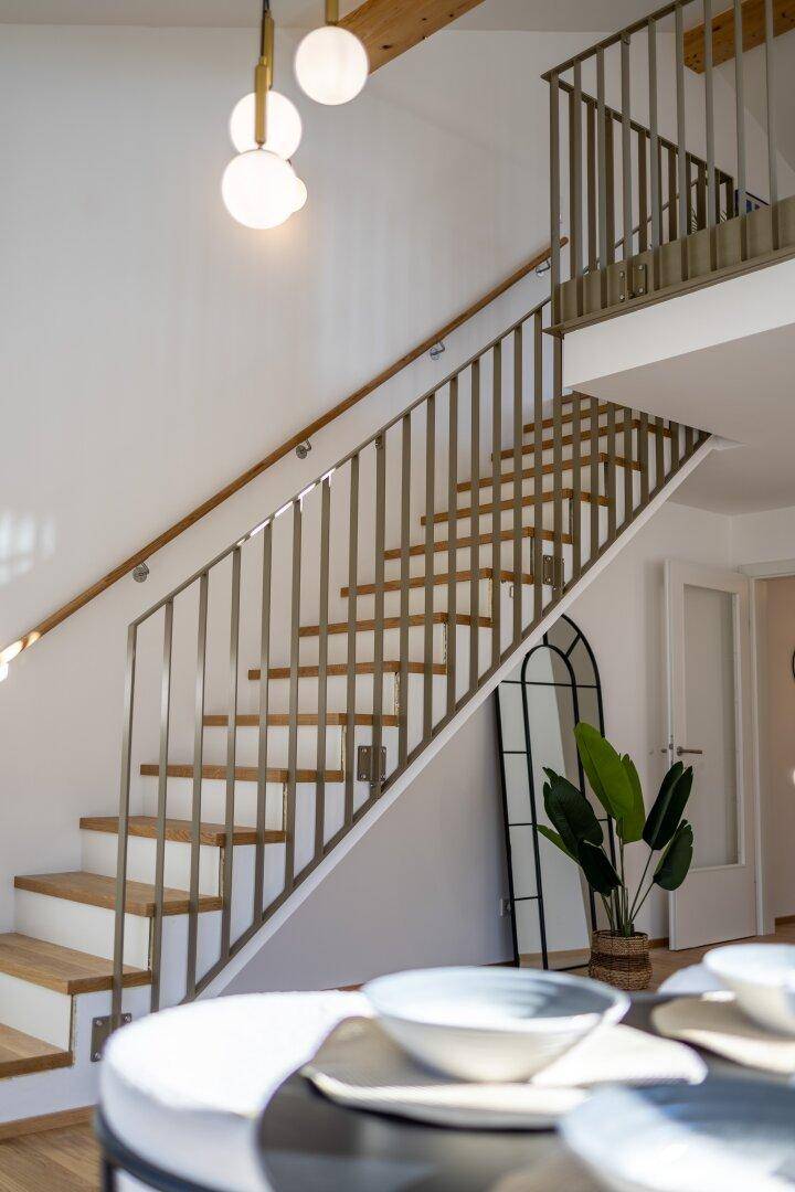 Moderne Holztreppe mit Metallgeländer führt zur oberen Galerie.