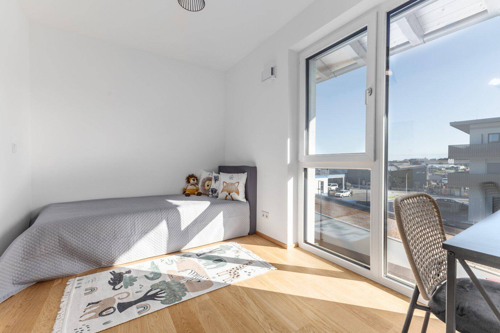 Kinderzimmer mit Holzboden, großem Fenster und Blick ins Grüne.