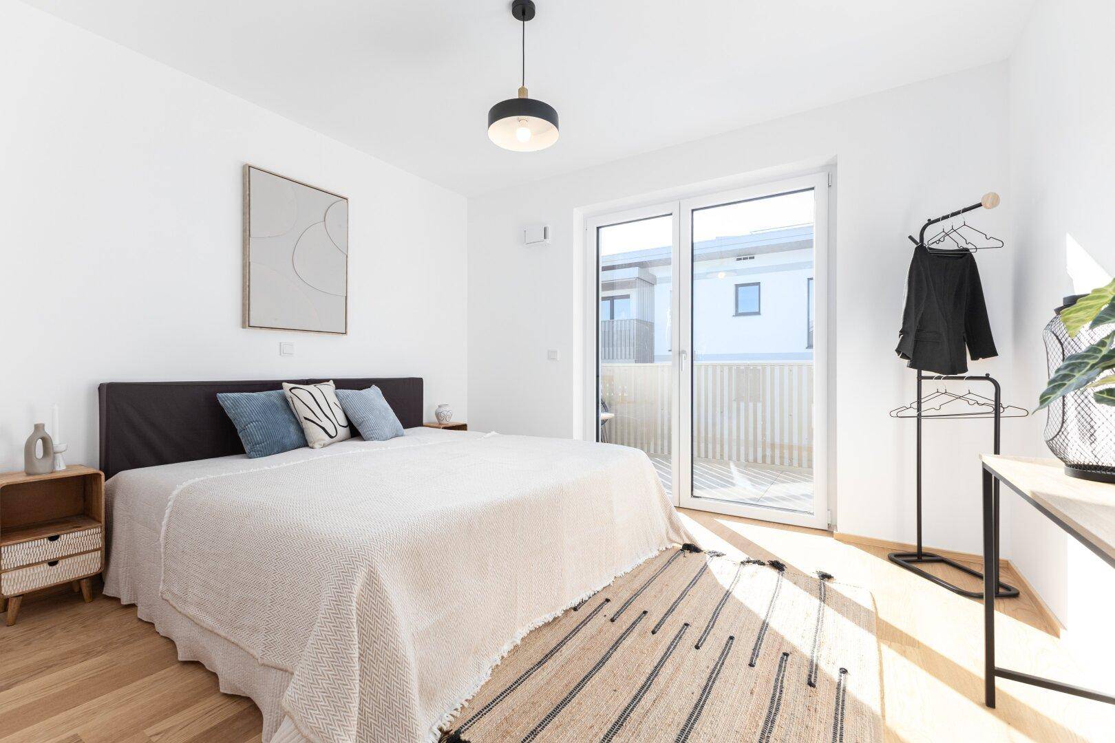 Helles Schlafzimmer mit Balkonzugang, Holzboden und moderner Einrichtung.