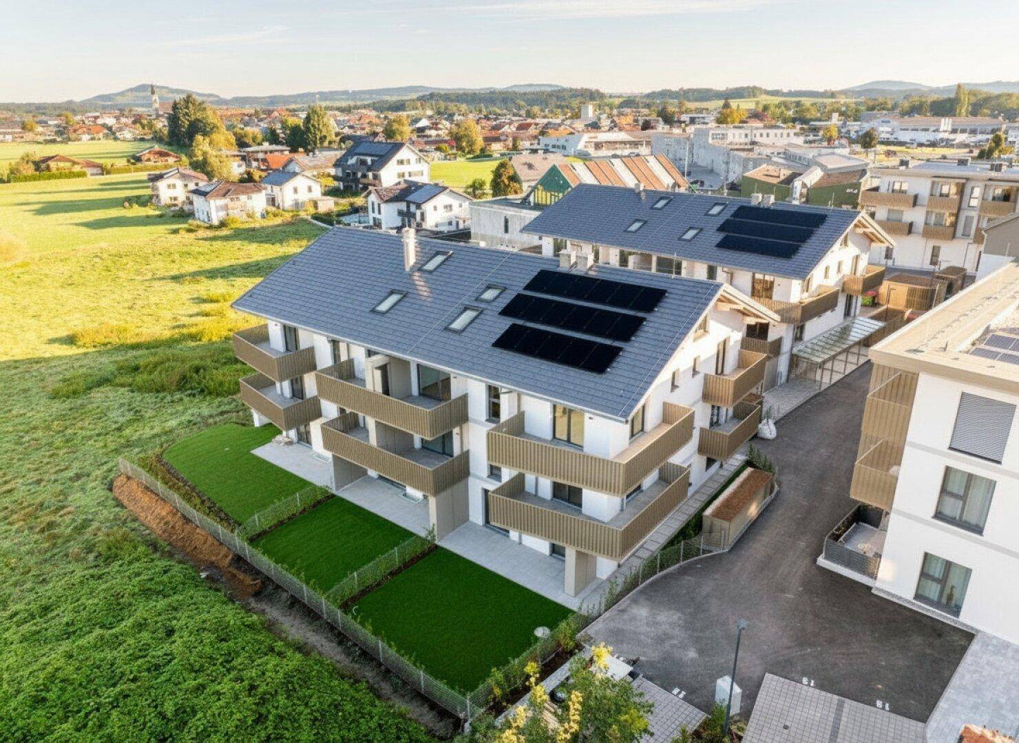 Neubauwohnanlage mit modernen Gebäuden, Balkonen und Photovoltaikanlagen auf den Dächern.